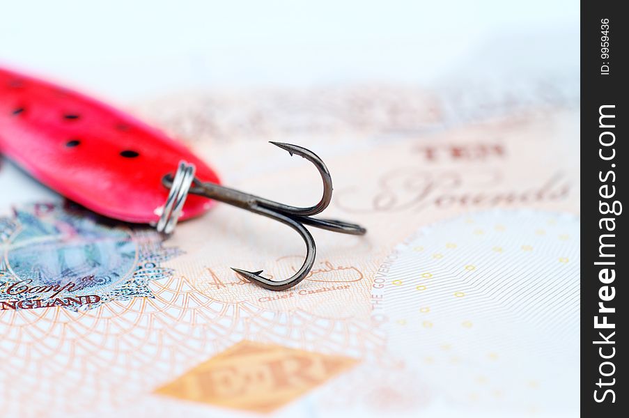 Close-up of fishing hook resting on UK bank note. Close-up of fishing hook resting on UK bank note