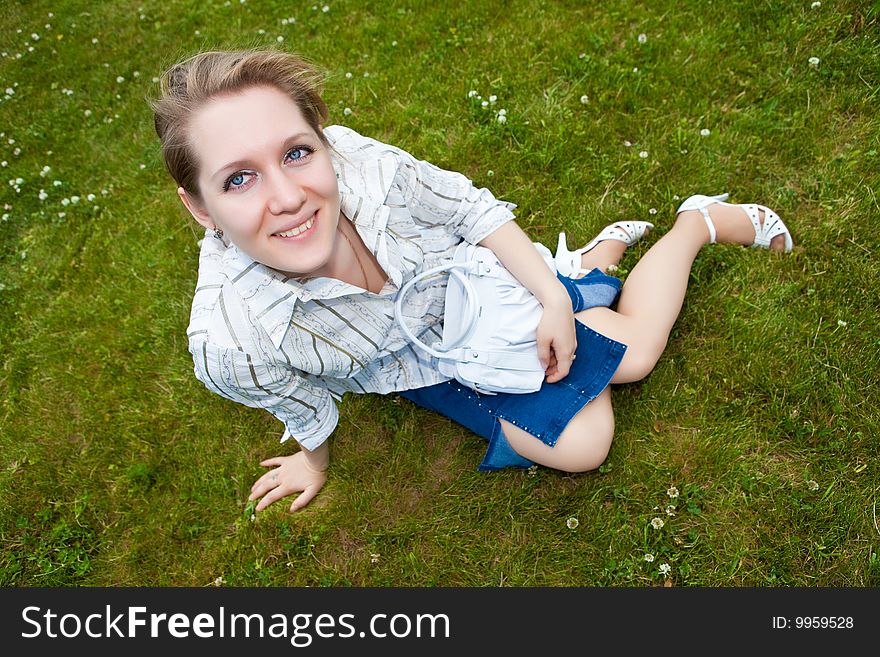 Beautiful young woman sits on a green grass