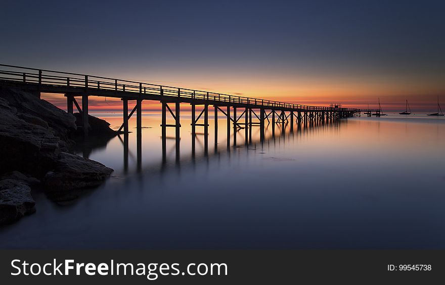 Sunset over wooden pier reflecting in calm waters.