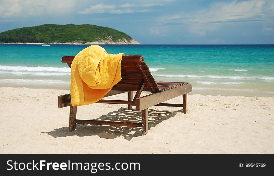 An empty wooden sunbed with a yellow towel on a sandy beach. An empty wooden sunbed with a yellow towel on a sandy beach.