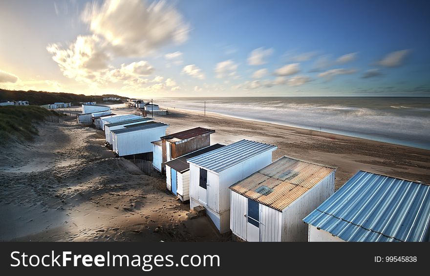 Row of changing huts built on sand dunes close to the beach and ocean, blue sky and fluffy clouds. Row of changing huts built on sand dunes close to the beach and ocean, blue sky and fluffy clouds.