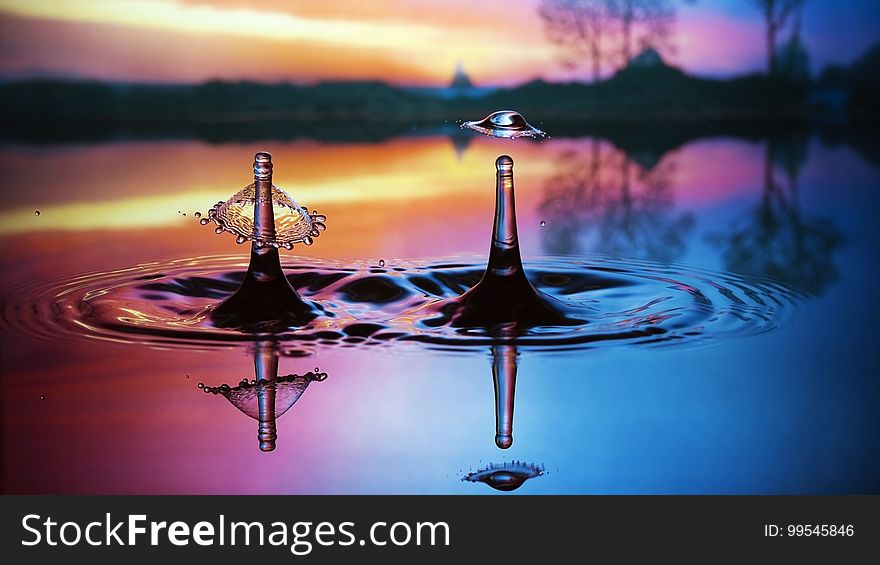 Two water splashes reflecting on colorful pool outdoors at sunset. Two water splashes reflecting on colorful pool outdoors at sunset.