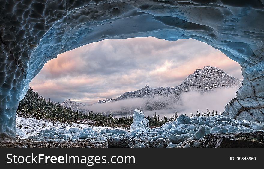 A frozen cave and a view of rocky mountain peaks in the background.