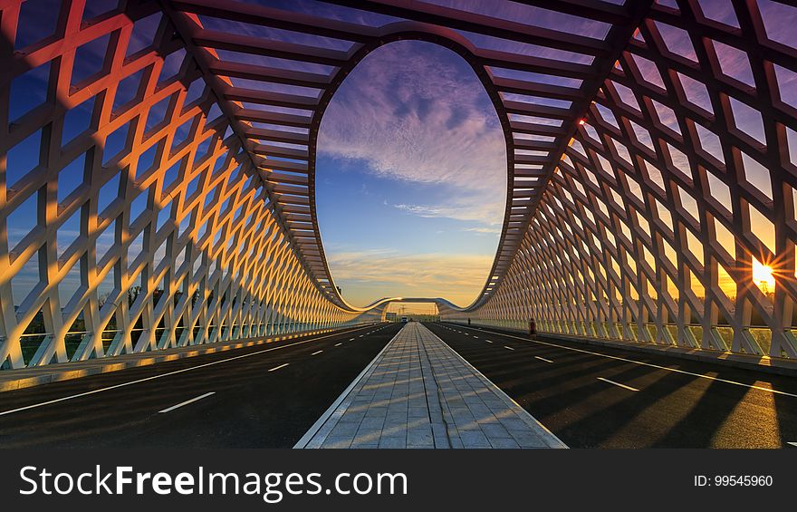 Two lanes receding over modern road bridge with unique architectural design at sunset. Two lanes receding over modern road bridge with unique architectural design at sunset.