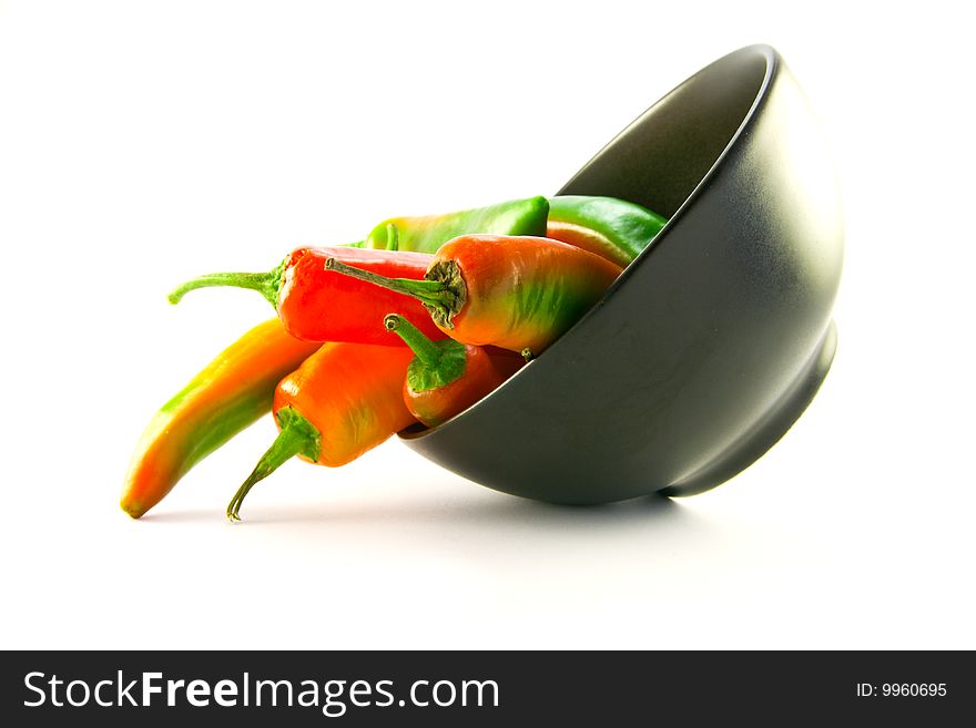 Mixed red and green chillis spilling out of a black bowl with clipping path on a white background