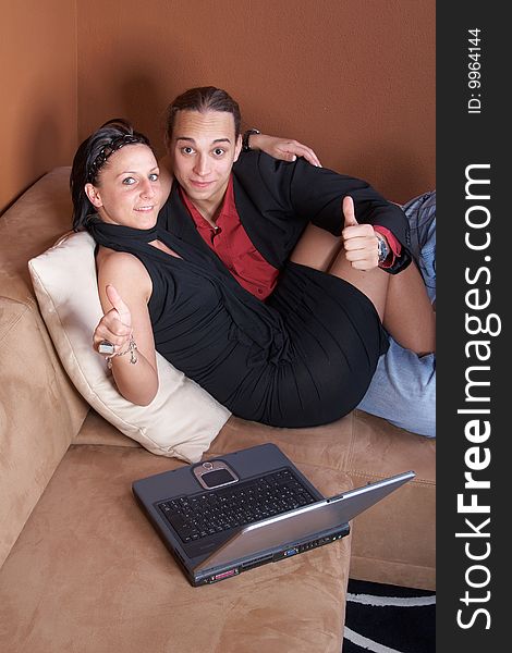 Young couple on the couch surfing the web with their laptop - showing a thumbs up sign. Young couple on the couch surfing the web with their laptop - showing a thumbs up sign.