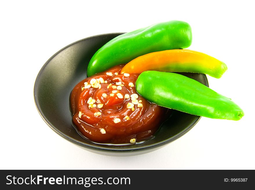 Whole chillis in a black bowl with red chilli dipping sauce with clipping path on a white background. Whole chillis in a black bowl with red chilli dipping sauce with clipping path on a white background