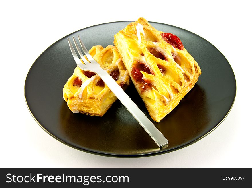 Raspberry and custard danish on a black plate with a fork on a white background. Raspberry and custard danish on a black plate with a fork on a white background