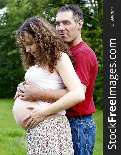A happy, young pregnant couple sharing an embrace with exposed belly.