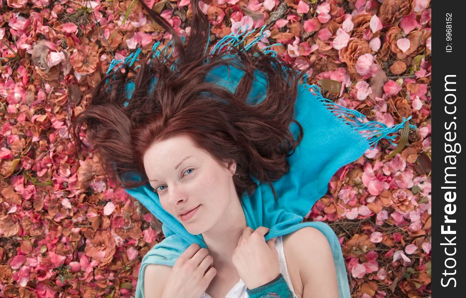 Young woman laying on ground on blue scarf on ground covered with pink petals. Shallow depth of field. Young woman laying on ground on blue scarf on ground covered with pink petals. Shallow depth of field.