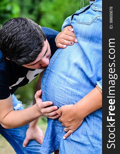 Happy and young pregnant couple hugging near a lake