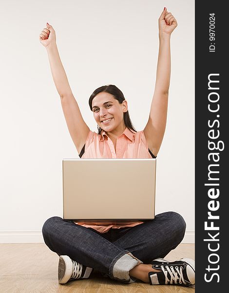 Young woman seated on floor with laptop and arms raised with excitement. Young woman seated on floor with laptop and arms raised with excitement