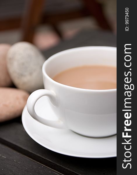 Outdoor cup of tea in a white cup and saucer with stones on a wooden background