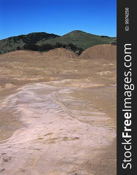 Brown volcano with green hills and blue sky in background