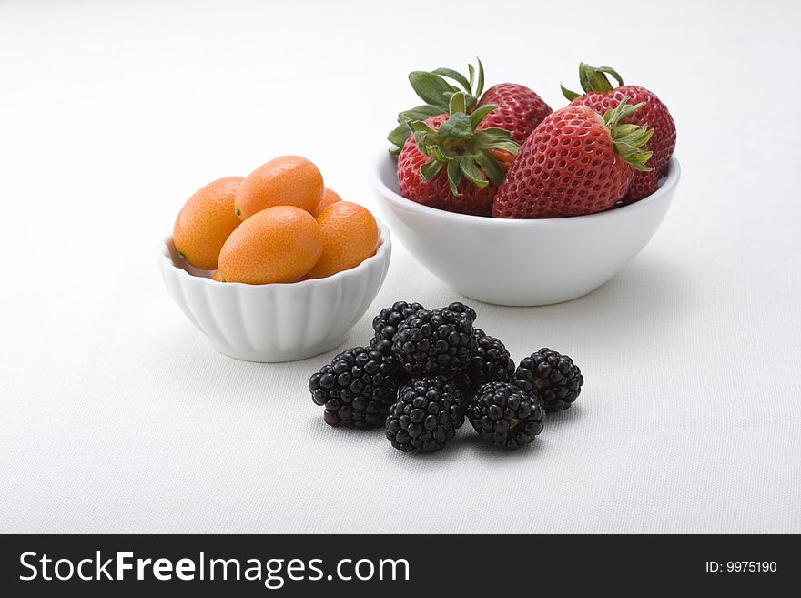 Bowls of delicious strawberries, kumquats, and blackberries at the peak of freshness. Bowls of delicious strawberries, kumquats, and blackberries at the peak of freshness