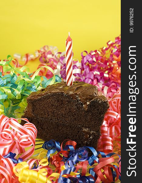 A piece of delicious homemade chocolate cake with one candle and party decorations, vertical with copy space. A piece of delicious homemade chocolate cake with one candle and party decorations, vertical with copy space