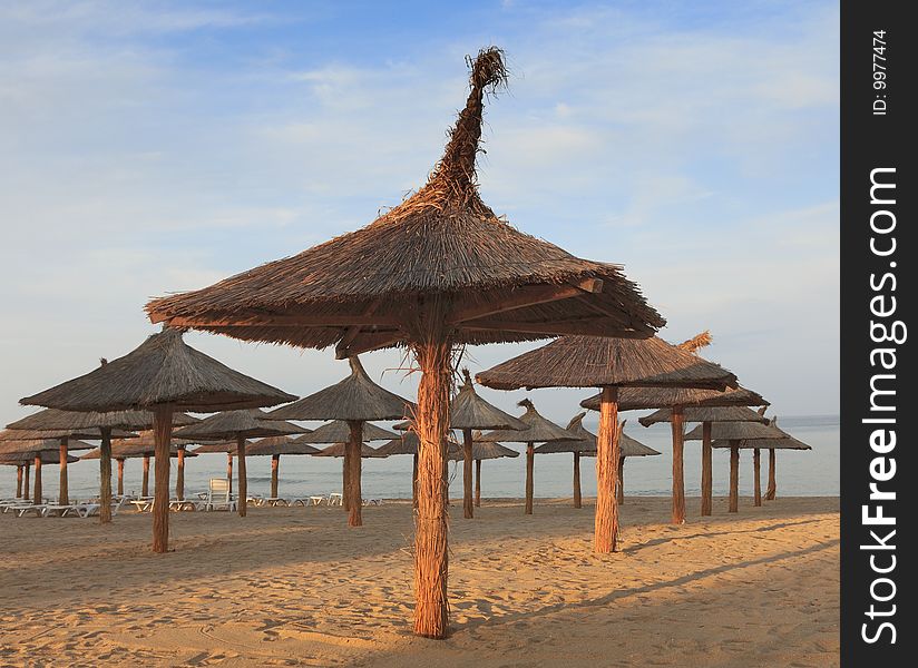 Thatched parasols on a tropical beach at sunset.
