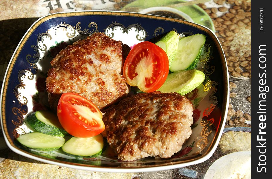 Cutlets in a plate with cucumbers and tomatoes on a table