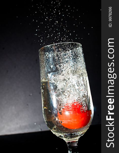 Juicy tomato dropped into a glass full of water creating splashes of water droplets. Juicy tomato dropped into a glass full of water creating splashes of water droplets.