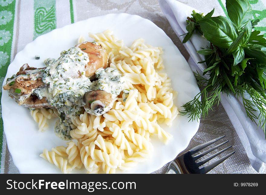 Chicken legs with pasta with herbal cream sauce, arranged with a bunch of fresh greens on a white napkin