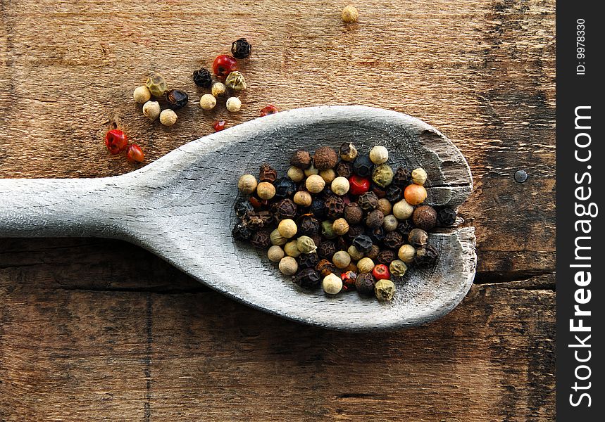 Peppercorns of various colors on a wooden spoon and a rustic surface. Peppercorns of various colors on a wooden spoon and a rustic surface.