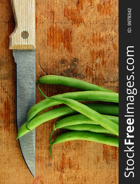 Fresh green beans and a knife on a rustic wooden table. Fresh green beans and a knife on a rustic wooden table.