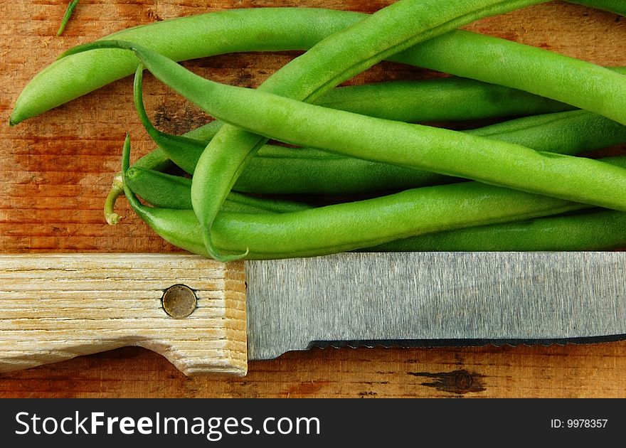 Fresh green beans and a knife on a rustic wooden table. Fresh green beans and a knife on a rustic wooden table.