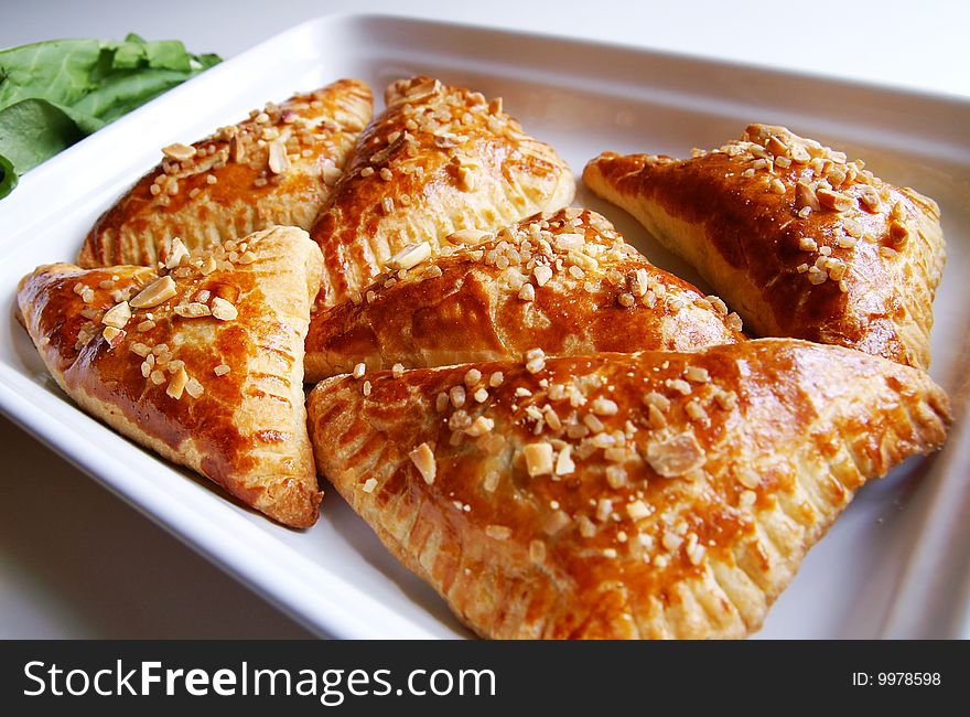 A white dish with baked puff-pastry pasties filled in fresh sorrel with sugar and peanut, blur background