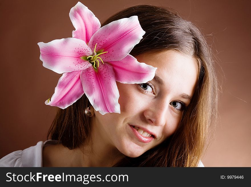 A pretty young woman with long brown hair posing with a pink lily near her face. A pretty young woman with long brown hair posing with a pink lily near her face