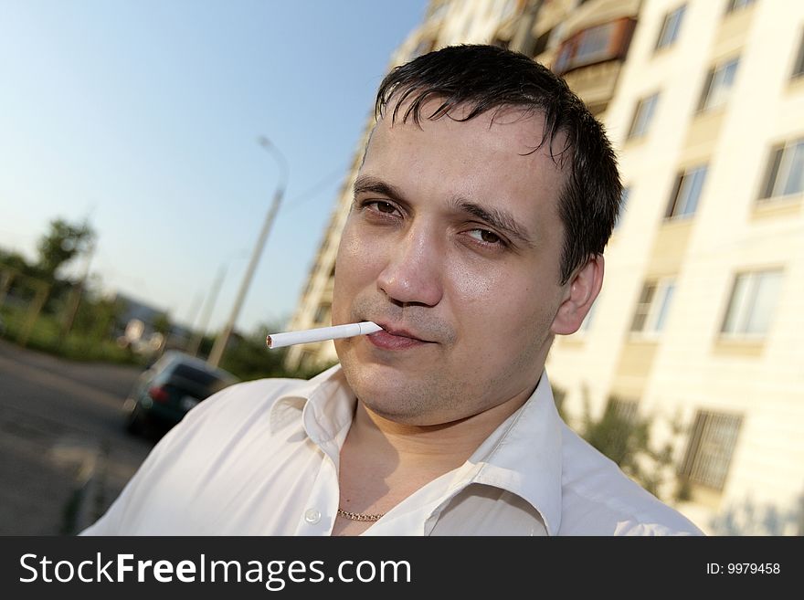 The man with a cigarette poses outdoor. The man with a cigarette poses outdoor