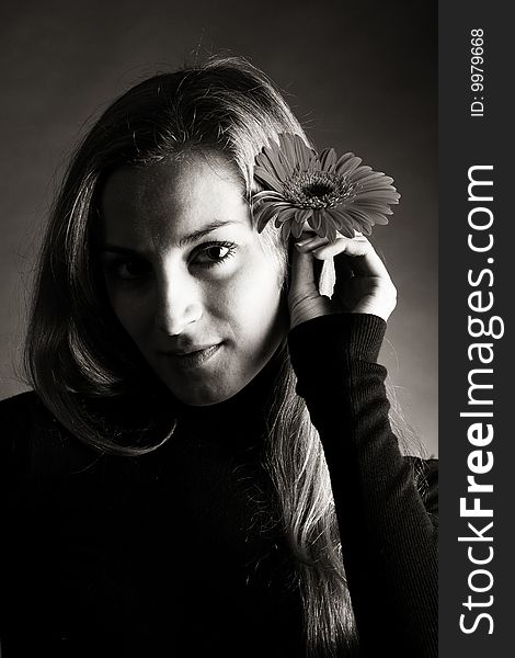 A young beautiful girl in dark  jumper posing with a flower in her hand. A young beautiful girl in dark  jumper posing with a flower in her hand