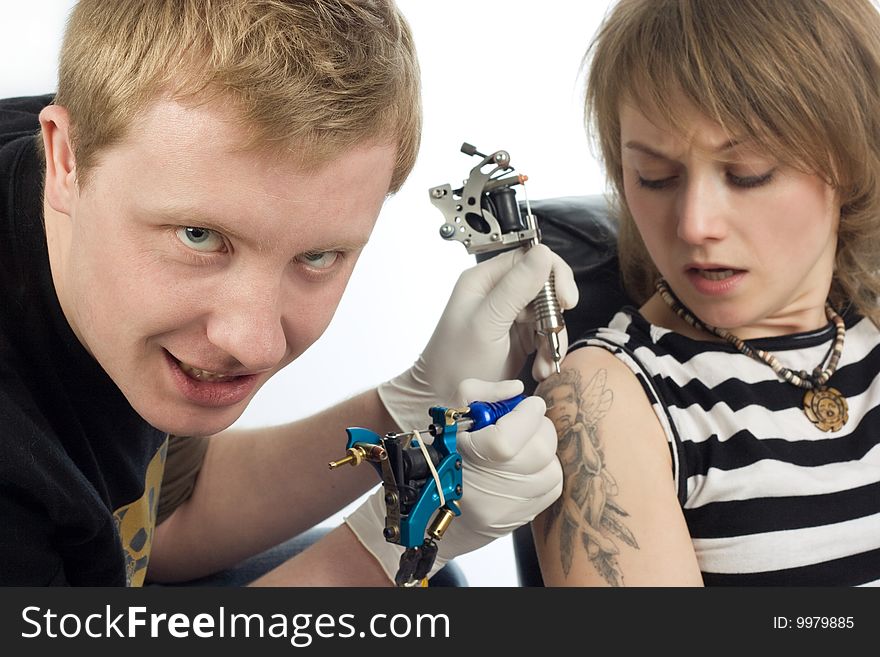 An image of a man making tattoo to a scared woman. An image of a man making tattoo to a scared woman