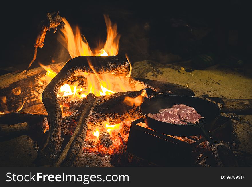 Close up of burning campfire with cast iron skillet full of meat at night. Close up of burning campfire with cast iron skillet full of meat at night.