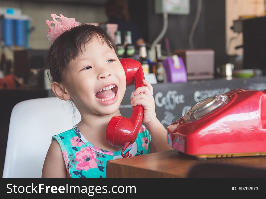 Little asian girl smiling while talking with her friend by red classic phone. Little asian girl smiling while talking with her friend by red classic phone