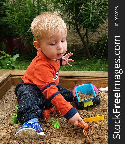 A small boy playing with sand and plastic toys.