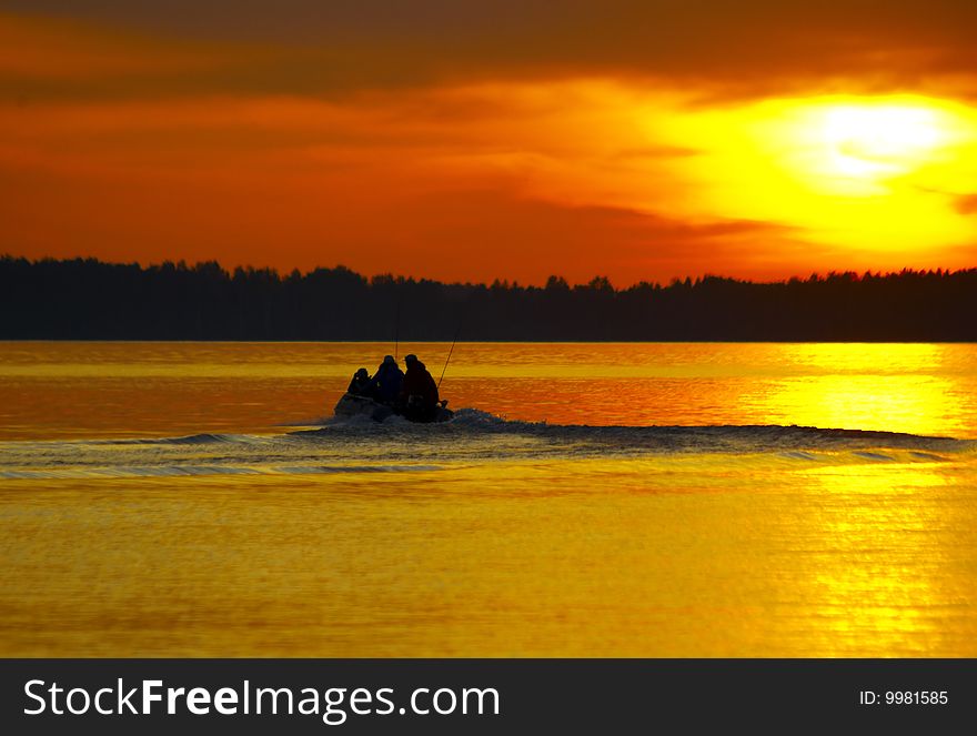 Sunset and motor boat with three persons going to fish