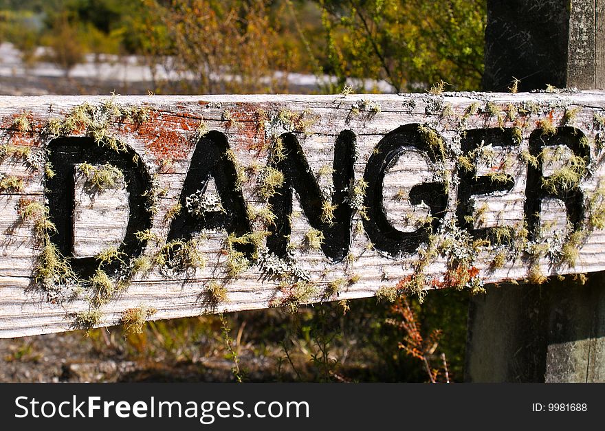 Old wooden danger sign covered by moss