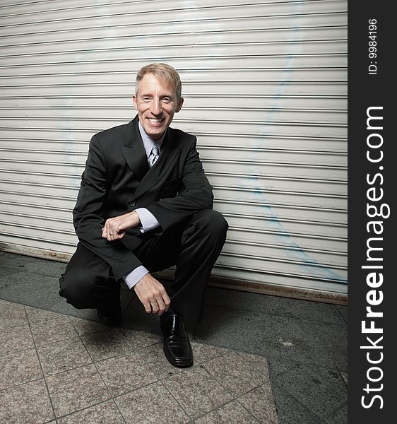 Mature businessman squatting and smiling