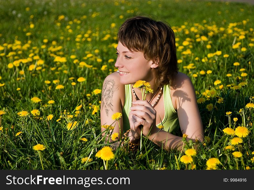 A young cheerful woman having fun on a dandelions glade