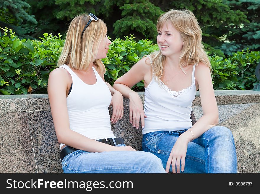 Two girls talk sitting on a bench in park. Two girls talk sitting on a bench in park