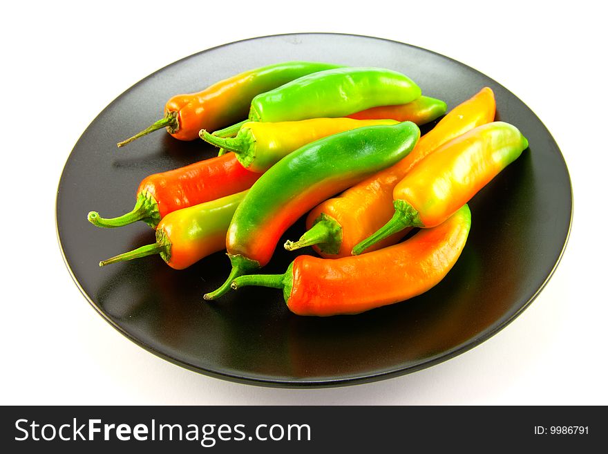 Red, green and yellow whole chillis on a black plate with clipping path on a white background. Red, green and yellow whole chillis on a black plate with clipping path on a white background