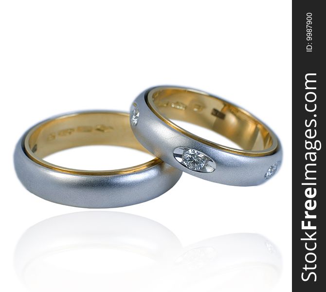 His and hers golden wedding bands, with diamonds. On a white background with soft reflection, isolated. His and hers golden wedding bands, with diamonds. On a white background with soft reflection, isolated.