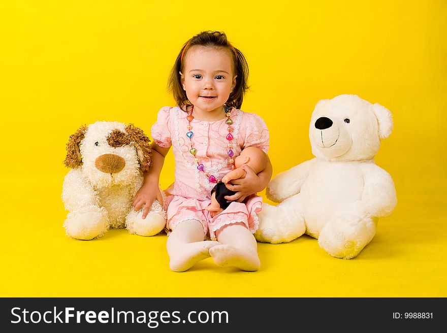 Cute little girl with toys on the floor over yellow.