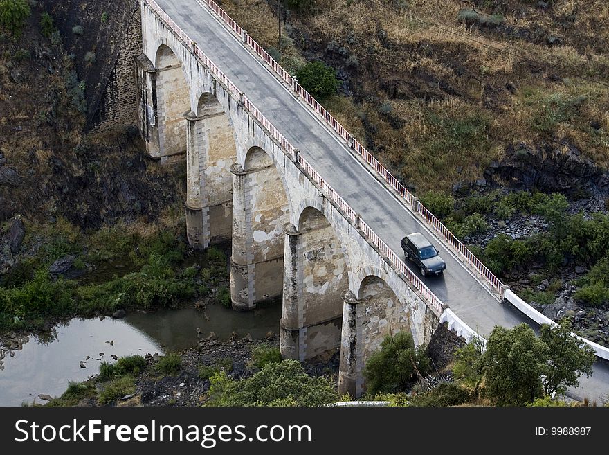 Top view of a arc stoned bridge over a river with a car passing by. Top view of a arc stoned bridge over a river with a car passing by.