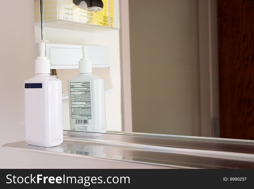 A bottle of hand soap setting on a shelf by a mirror