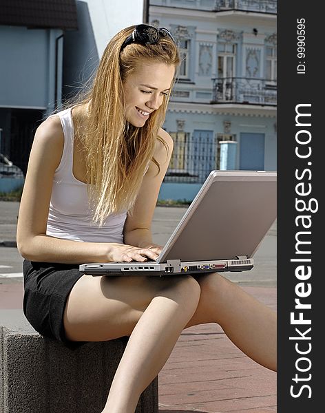 Happy blonde collegian using laptop outside educational institution. Happy blonde collegian using laptop outside educational institution