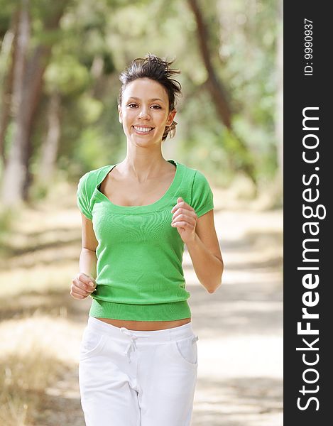 Young woman jogging in green forest, smiling and looking in camera. Young woman jogging in green forest, smiling and looking in camera