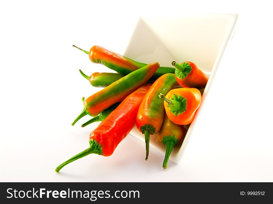Red and green chillis spilling out of a white square bowl with clipping path on a white background. Red and green chillis spilling out of a white square bowl with clipping path on a white background