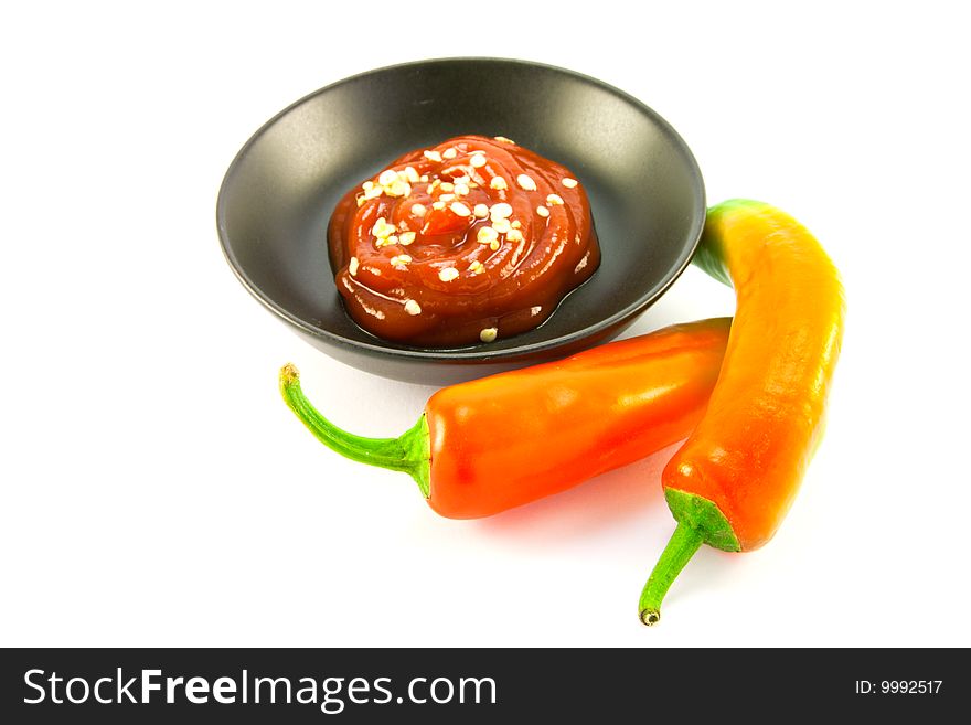 Two red chillis with small black bowl of chili dipping sauce with clipping path on a white background. Two red chillis with small black bowl of chili dipping sauce with clipping path on a white background