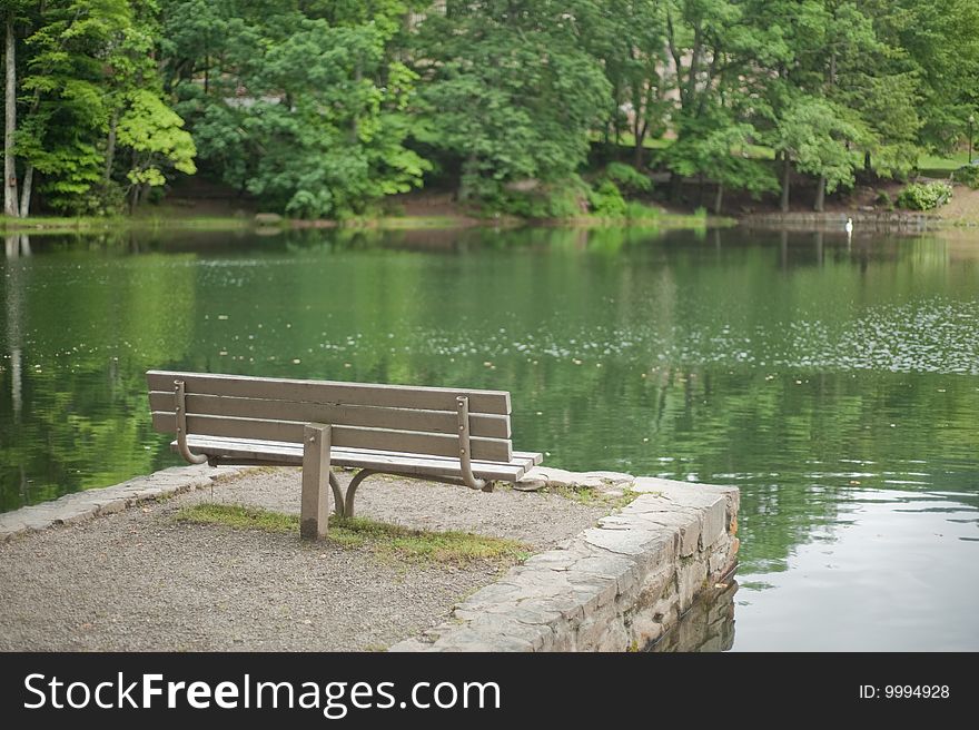 Empty wooden park bench sitting by the lake in the summer time. Empty wooden park bench sitting by the lake in the summer time